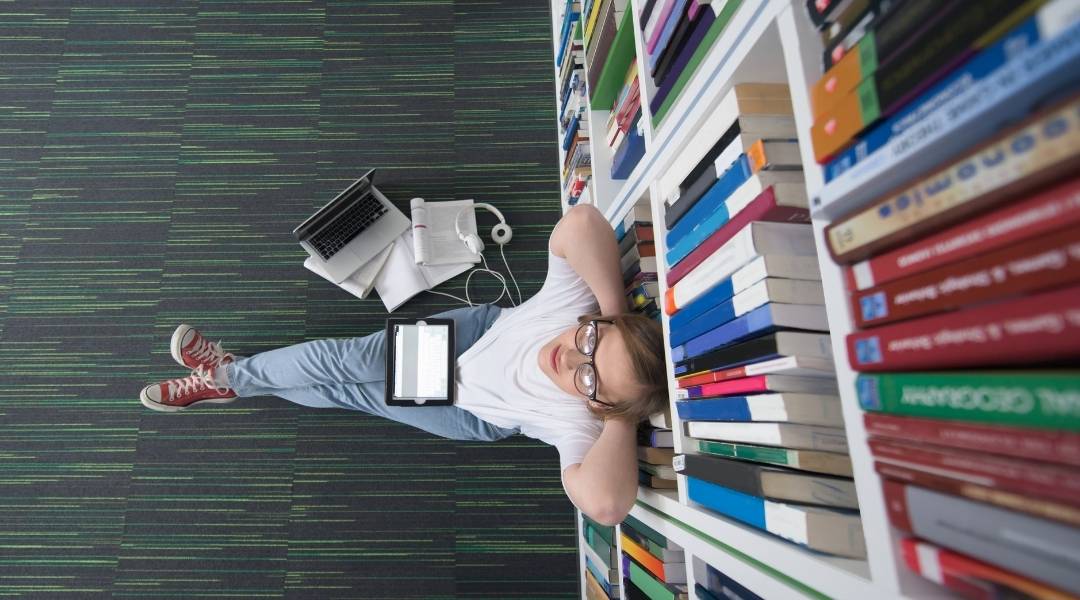 Jovem descansando na biblioteca com um notebook no colo após ter estudado muito sobre o seguro D&O