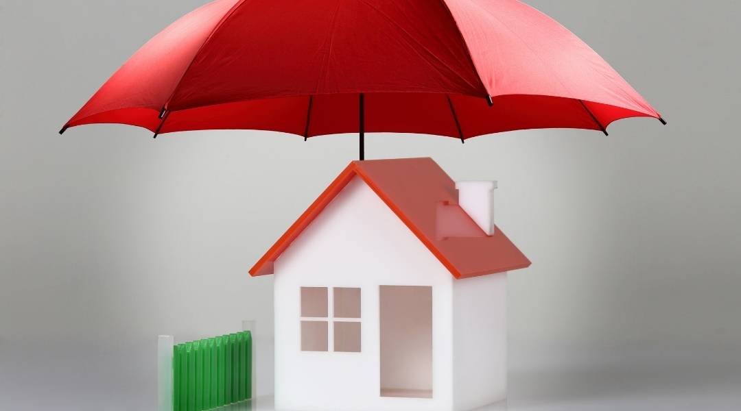 Pequena maquete de uma casa com um guarda-chuva vermelho em cima dela, vantagens de ter boas coberturas no seguro residencial