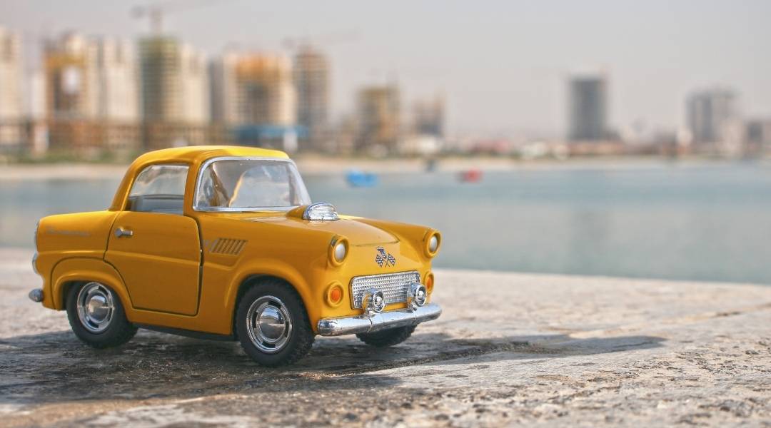 Carro em miniatura a beira de um porto. Atrás uma grande cidade desfocada. Valor do seguro de carro