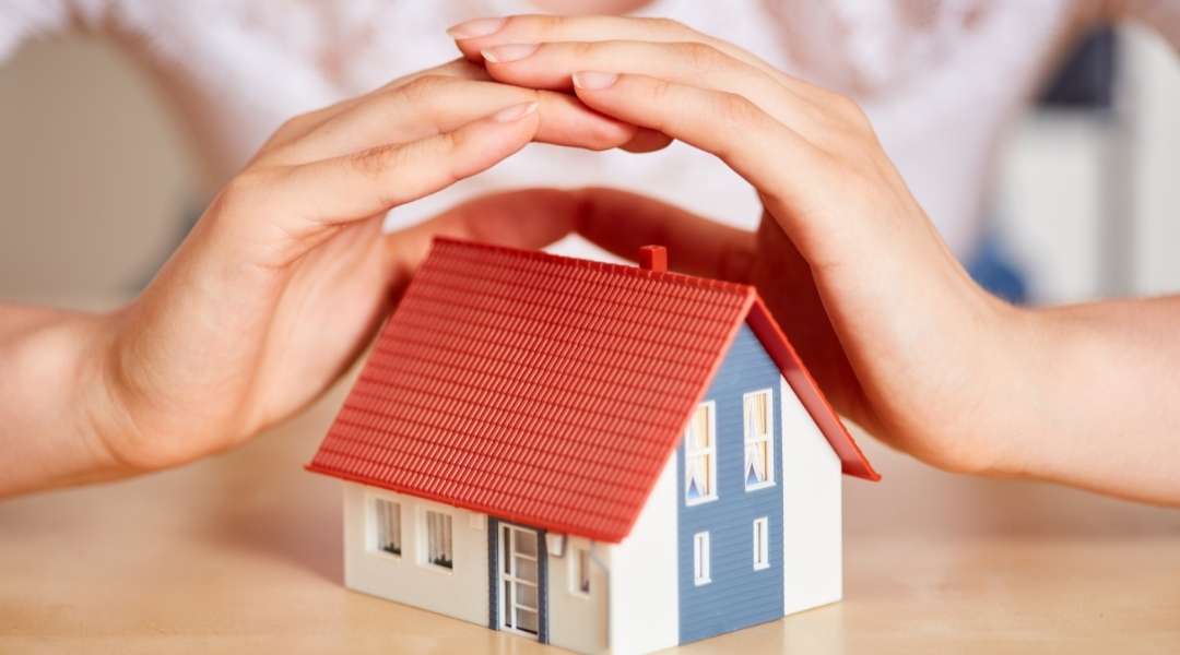 Duas mãos cobrindo uma casa em miniatura