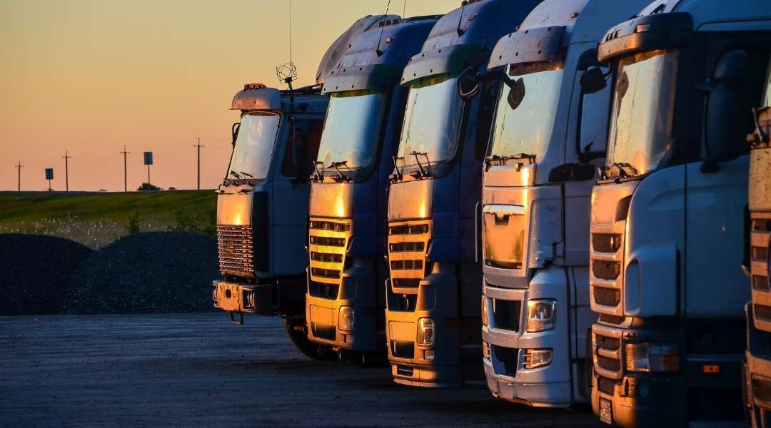 quatro caminhões lado a lado estacionados, pôr do sol no fundo. tipos de seguros